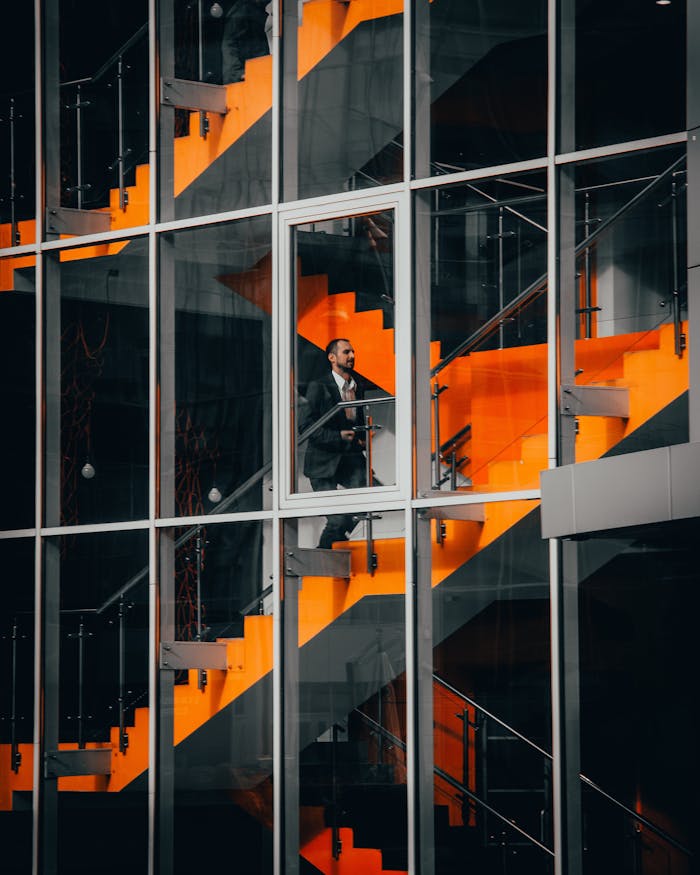 our-story A businessman in a suit walking on a striking orange staircase in a modern office building.