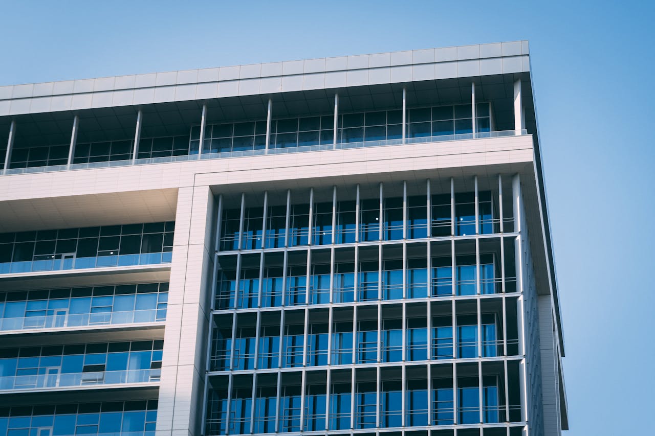 A modern high-rise office building with a distinctive glass facade under a clear blue sky.