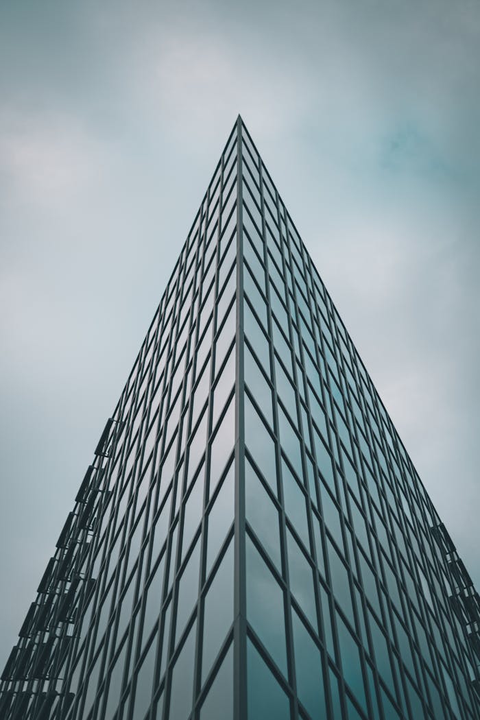 Low angle view of a modern skyscraper with reflective glass panels against a cloudy sky.